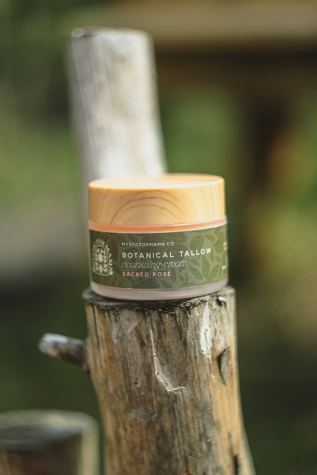 A small jar of Botanical Fatty Hair Repair Cream sits on a rustic wooden post in an outdoor setting with a blurred green background.