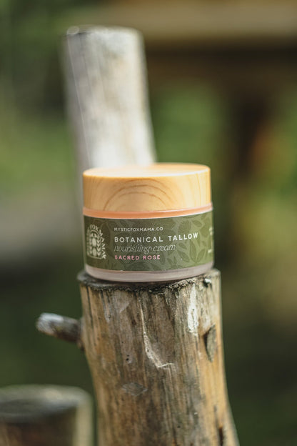 A small jar of Botanical Fatty Hair Repair Cream sits on a rustic wooden post in an outdoor setting with a blurred green background.