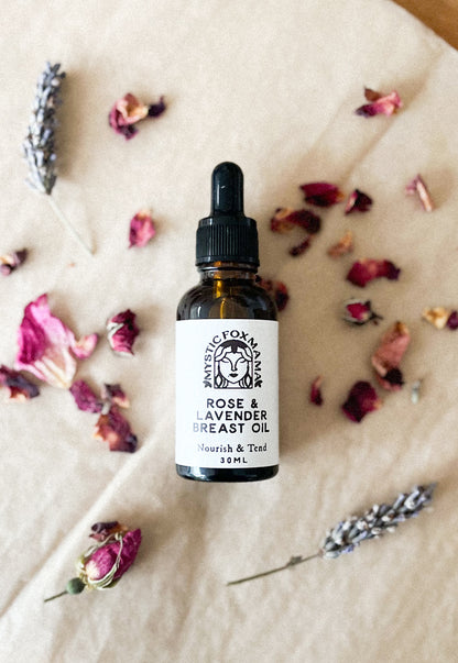 A small bottle of 'Rose & Lavender Breast Oil' with a dropper, placed on a surface with rose petals and lavender sprigs around it.