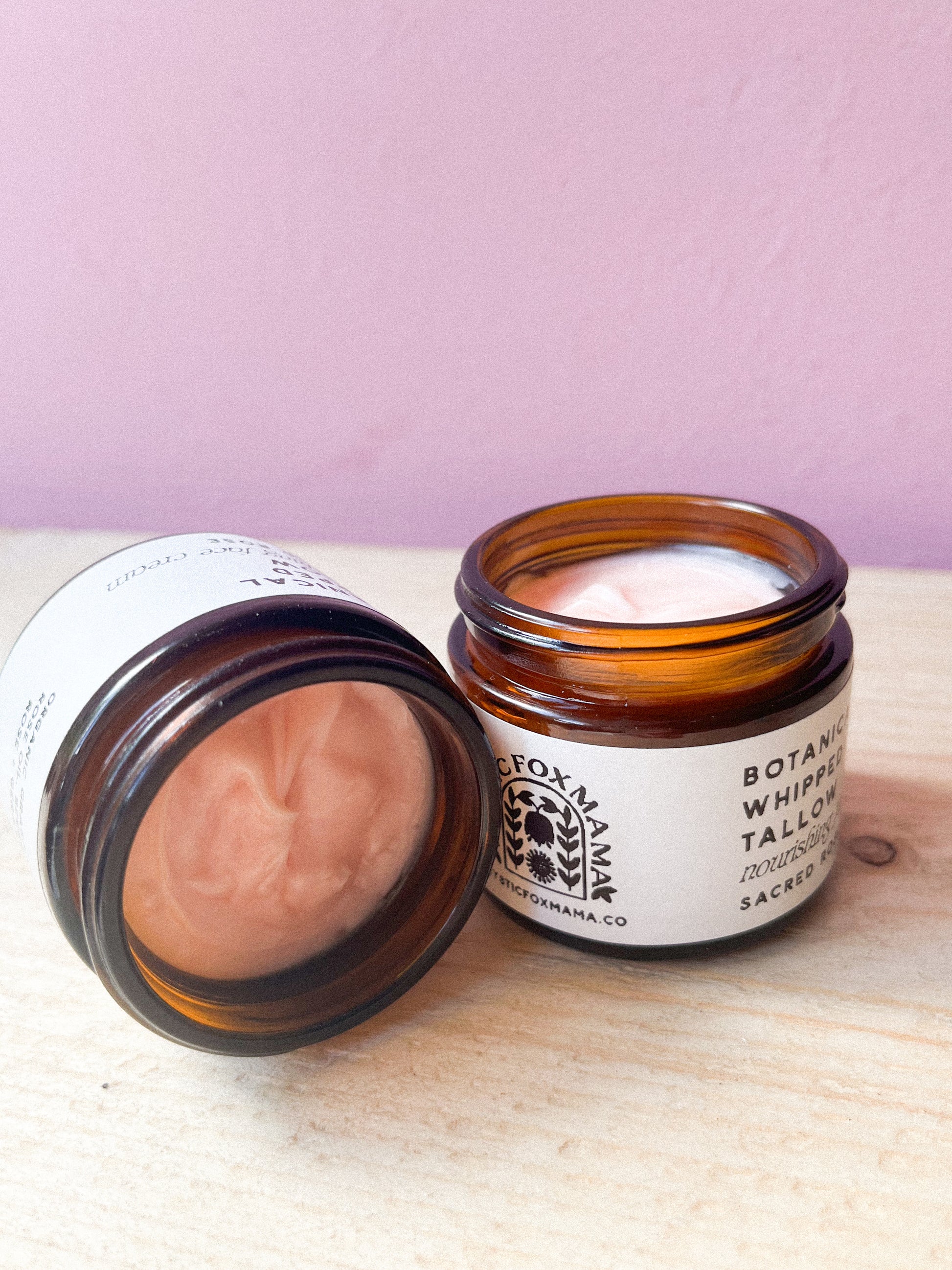 Two open jars of a cosmetic product on a wooden surface with a pink background