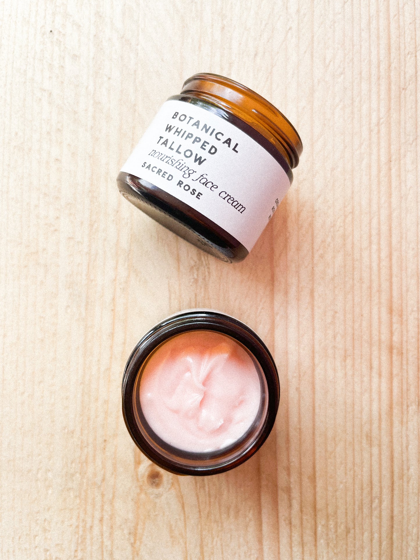 Two jars of botanical whipped tallow face cream on a wooden surface